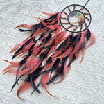 Capteur de rêves décoratif en plumes rouges et noires suspendu sur un fond en dentelle blanche.