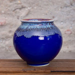Un pot en céramique de couleur bleu foncé avec des motifs texturés sur le pourtour, posé sur une surface en bois.