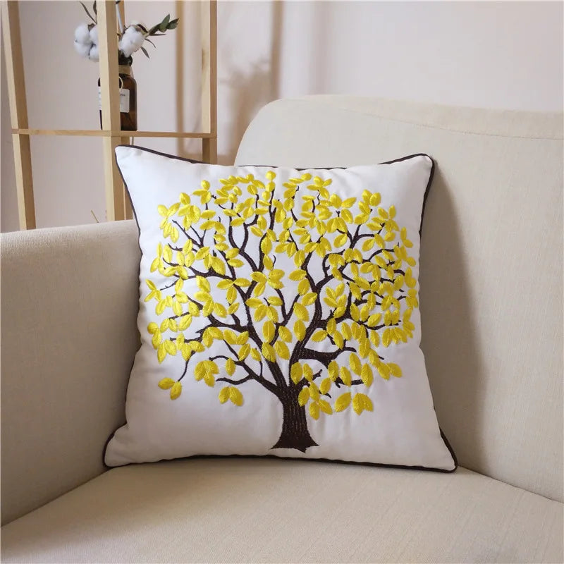 Coussin décoratif avec un arbre aux feuilles jaunes brodées sur un fond blanc, créant une décoration de salon chaleureuse et naturelle.
