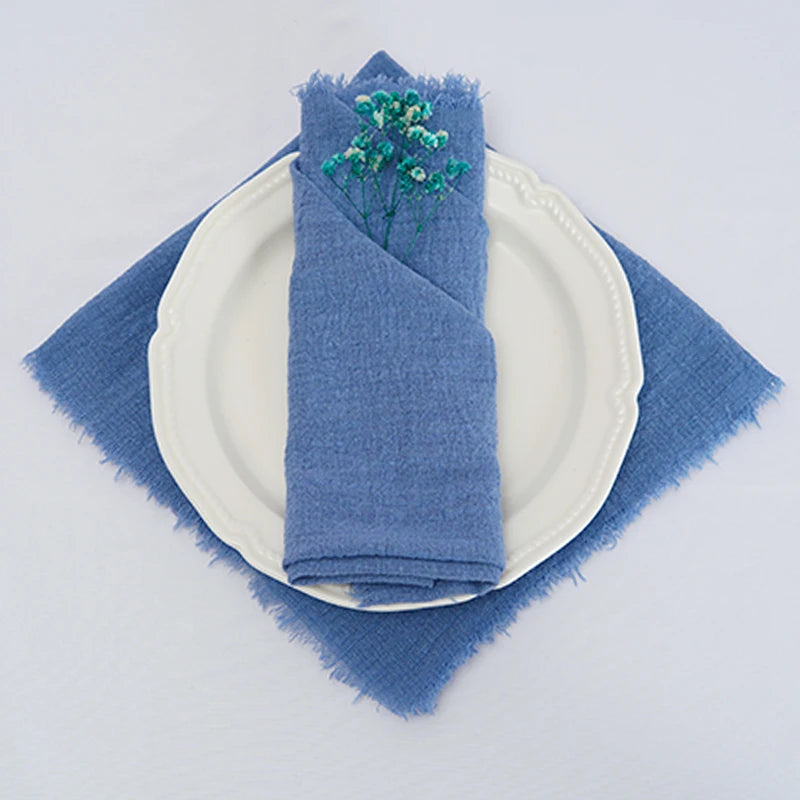 L'image montre une serviette en tissu bleu foncé enroulée autour d'une assiette blanche sur une nappe de table de couleur bleue.