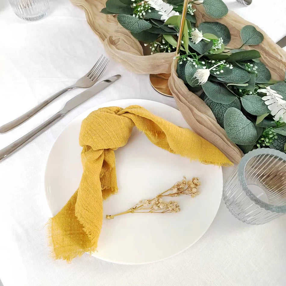Assiette blanche avec serviette en tissu jaune et fleurs séchées, sur une table avec des couverts et un centre de table floral.