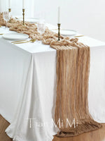 Cette table de salle à manger élégante est décorée avec un chemin de table en tissu beige décoratif, des chandeliers et des assiettes blanches sur un fond blanc, créant une ambiance chaleureuse et raffinée.