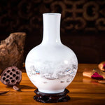 Vase en porcelaine blanche avec motif de paysage de montagne sous la neige, posé sur un support en bois foncé.