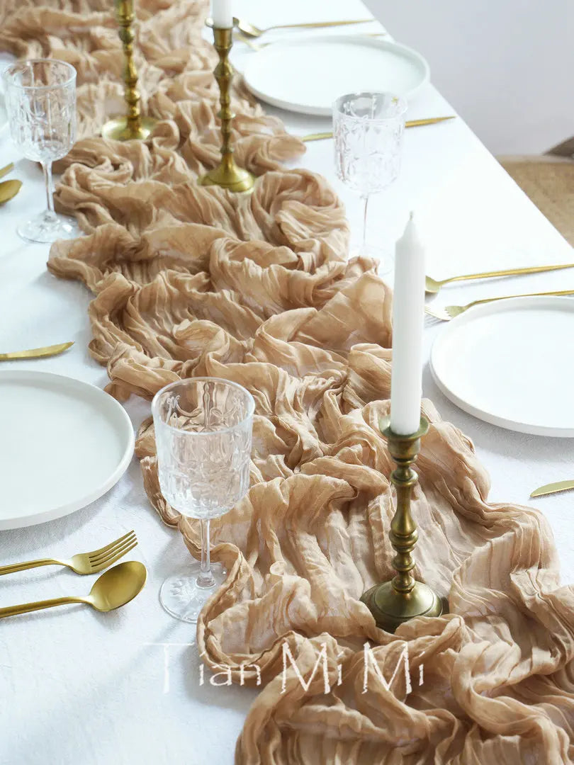 Table de banquet élégante avec nappe en voile crème, vaisselle blanche, verres en cristal et accessoires dorés, créant une ambiance sophistiquée et raffinée.
