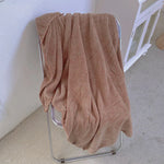 Une couverture en tricot beige, douce et confortable, est suspendue sur un support métallique.