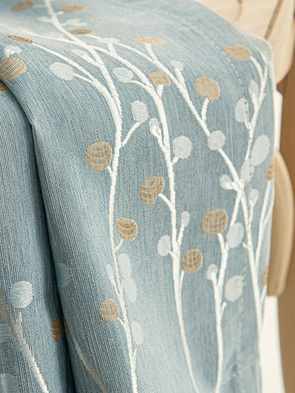 Détail du tissu d'un rideau occultant bleu en polyester avec motif floral brodé beige et blanc.