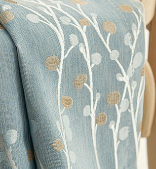Détail du tissu d'un rideau occultant bleu en polyester avec motif floral brodé beige et blanc.