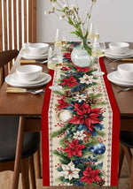 Cette image présente une belle composition de table avec une nappe à motifs floraux rouges et verts, des assiettes blanches, des verres à vin, un bouquet de fleurs dans un vase transparent et des couverts dorés, créant une ambiance chaleureuse et festive pour un repas.