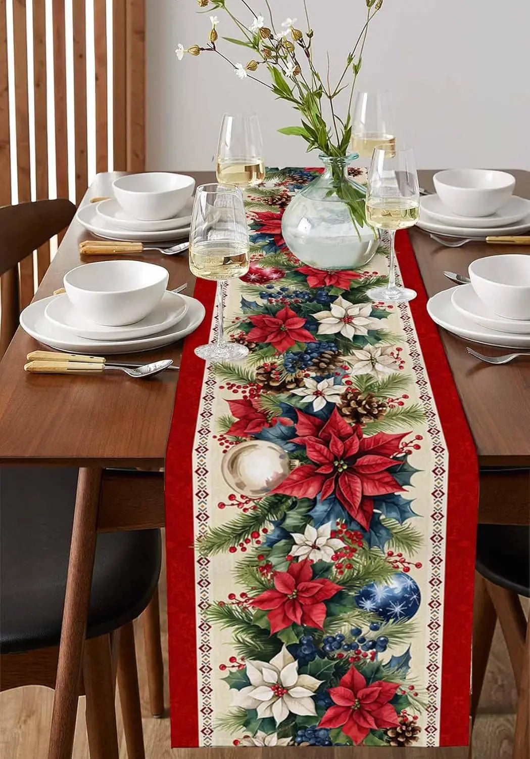 Cette image présente une belle composition de table avec une nappe à motifs floraux rouges et verts, des assiettes blanches, des verres à vin, un bouquet de fleurs dans un vase transparent et des couverts dorés, créant une ambiance chaleureuse et festive pour un repas.