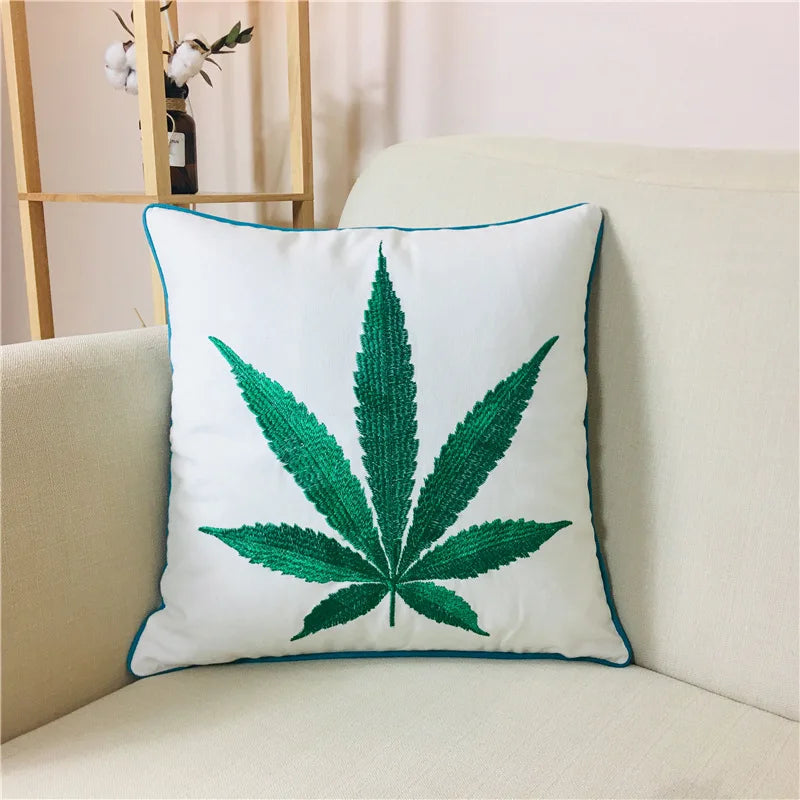 Coussin décoratif avec motif de feuille de cannabis imprimé, placé sur un canapé beige dans un intérieur lumineux.