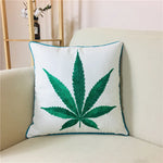 Coussin décoratif avec motif de feuille de cannabis imprimé, placé sur un canapé beige dans un intérieur lumineux.