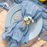 Une nappe bleue délicatement drapée, agrémentée d'une guirlande de fleurs de marguerite, confère une touche chaleureuse et naturelle à ce décor de table élégant.