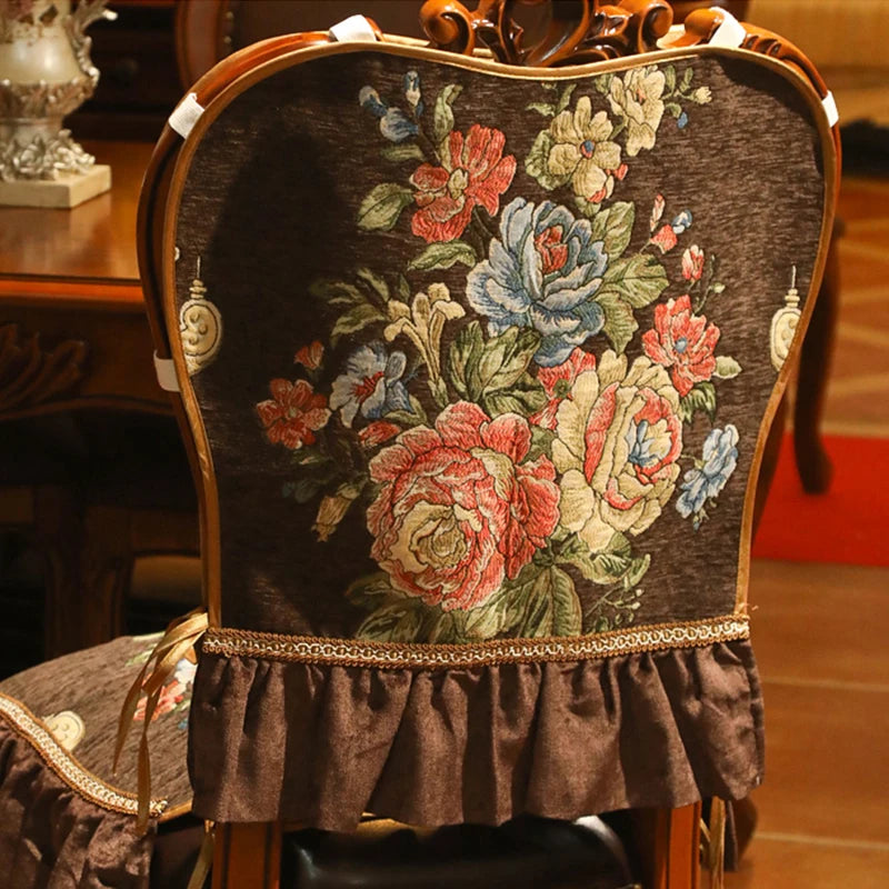 Le siège antique recouvert d'un superbe motif floral coloré, composé de roses épanouies, de fleurs bleues et blanches, sur un fond sombre, offrant une élégante décoration vintage.