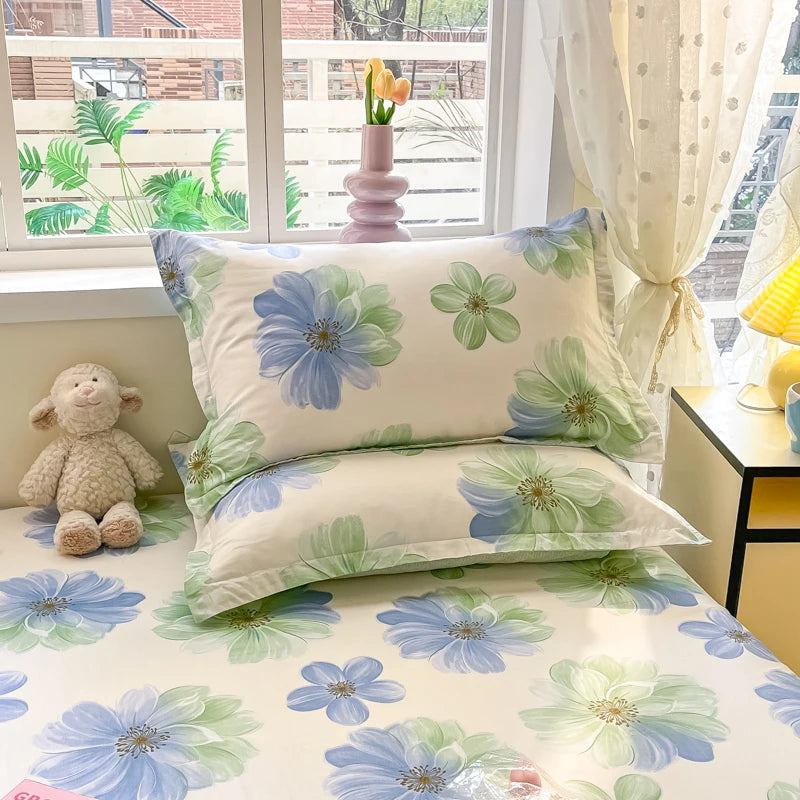 Ensemble de couverture de lit avec un motif de fleurs de couleurs pastel sur un fond clair, accompagné d'un vase rose et d'un ours en peluche sur le rebord de la fenêtre.