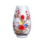 Vase en porcelaine avec motif de fleurs et de branches de prunier en couleurs vives sur fond blanc.