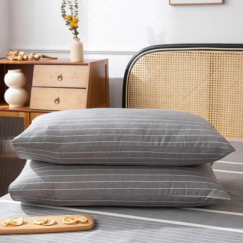 Des oreillers gris rayés reposent sur un lit dans une chambre avec du mobilier en bois et de la décoration florale.