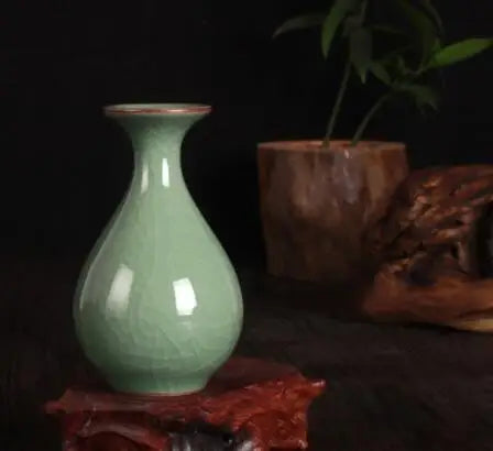 Un vase en céramique vert pastel, posé à côté de feuilles et d'un morceau de bois, crée une atmosphère apaisante et naturelle.