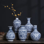 Un ensemble de vases décoratifs en porcelaine ornés de motifs bleus et blancs élégants, disposés sur une surface en bois sombre avec quelques branches de fleurs jaunes.