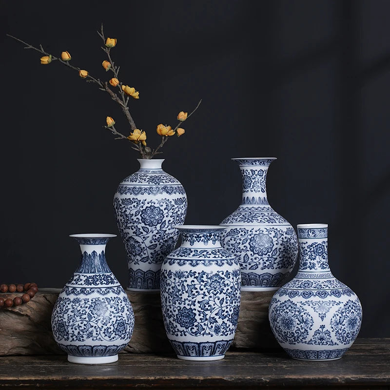 Un ensemble de vases décoratifs en porcelaine ornés de motifs bleus et blancs élégants, disposés sur une surface en bois sombre avec quelques branches de fleurs jaunes.