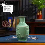 Un vase en céramique vert décoré de motifs de fleurs traditionnels sur un meuble en bois avec d'autres objets décoratifs en arrière-plan.