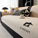 Un canapé beige avec des coussins et des décorations ornées du logo Elephant, une lampe dorée et un vase sur la table basse, dans un intérieur moderne et élégant.