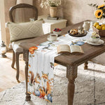 Cette table de petit-déjeuner chaleureuse et rustique met en scène une décoration automnale avec des fleurs, des fruits et un livre ouvert, créant une ambiance accueillante et cosy.