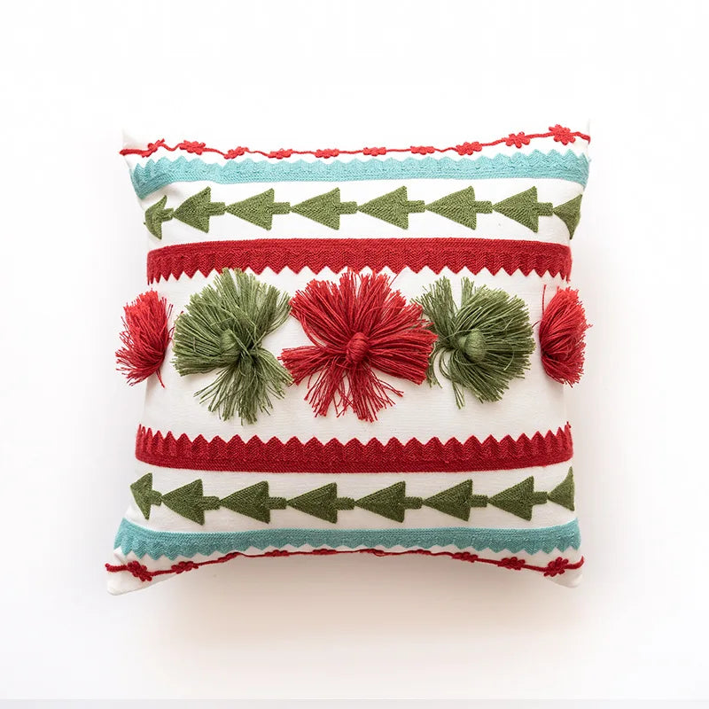 Coussin décoratif aux motifs géométriques et pompons rouges et verts sur fond blanc.