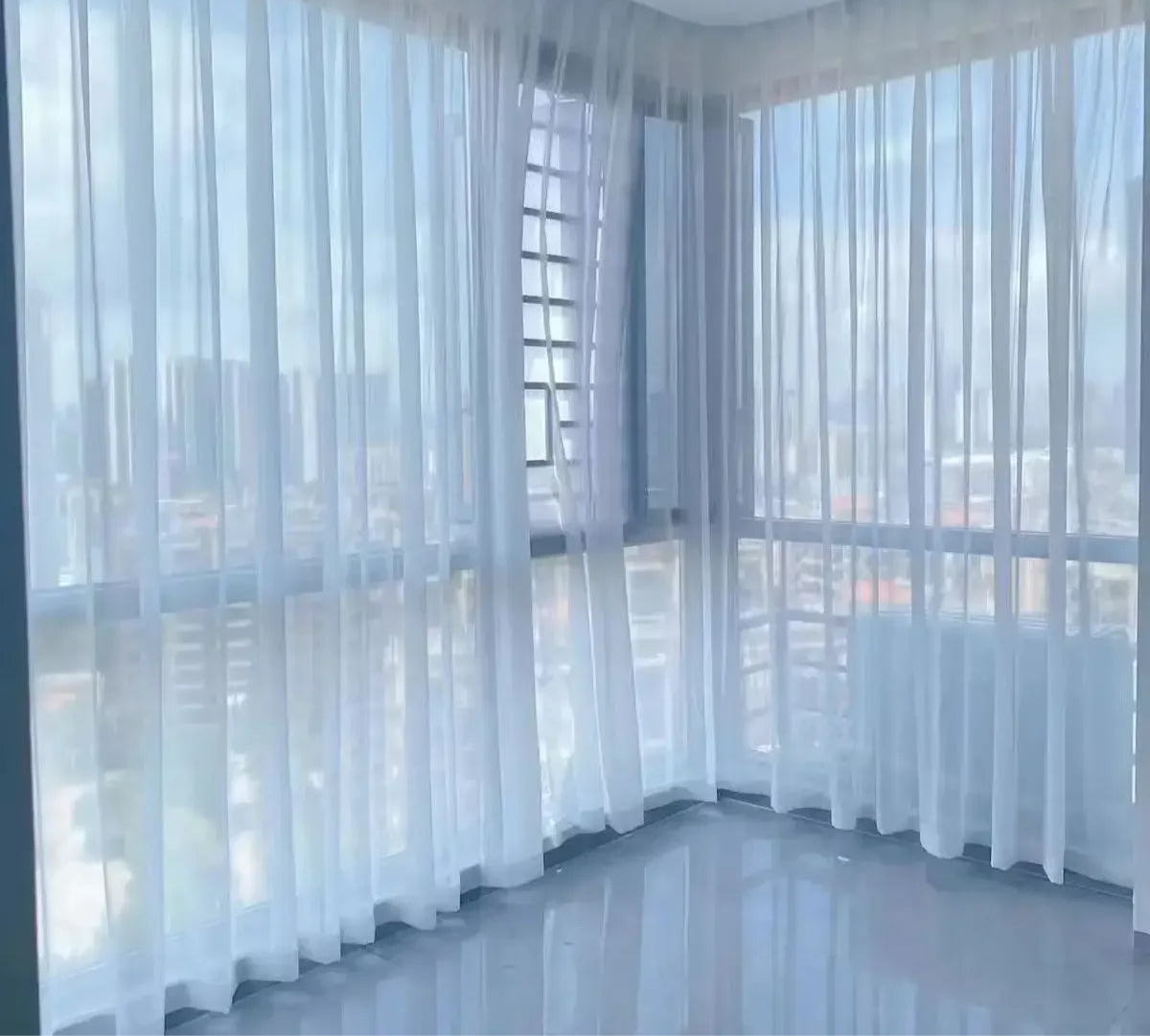 Rideaux en voile blanc sur baies vitrées d’angle avec vue sur la ville