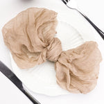 Un foulard chiffonné en tissu beige, enroulé et posé sur une surface blanche, avec une fourchette noire à côté.