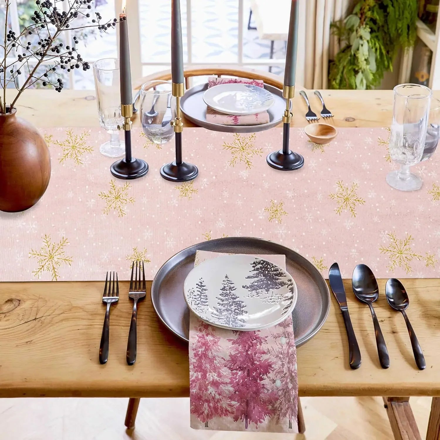 Une table de Noël élégante avec des candélabres noirs, des assiettes avec un motif forestier, des couverts noirs et une nappe blanche parsemée de flocons d'or.