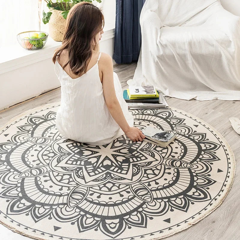 Une femme de dos assise sur un tapis rond avec un motif mandala noir et blanc dans une chambre lumineuse.