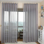 Rideaux élégants de couleur gris clair dans un salon contemporain, apportant une touche de sophistication et de modernité à la décoration intérieure. L'installation permet une diffusion idéale de la lumière naturelle tout en assurant une certaine intimité. Accessoires adjacents en harmonie avec le style lumineux et épuré.