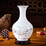 Vase en porcelaine blanche avec un design de paysage de montagne enneigé en trompe-l'œil, posé sur un support en bois sombre.