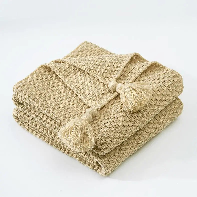 Une couverture en tricot beige dotée de pompons décoratifs.