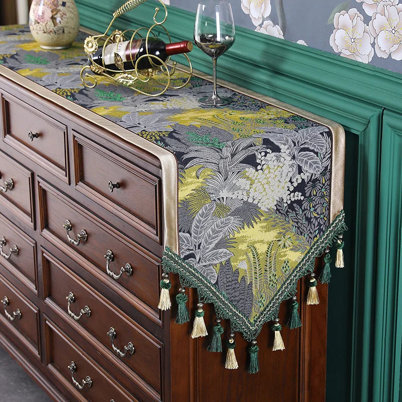 Commode en bois sombre avec un dessus recouvert d'un tissu floral bleu et vert, décoré d'un support à bouteille de vin et de verres à vin.