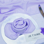 Une rose violette enveloppée dans un tissu délicat, accompagnée d'une étiquette avec l'inscription "Je t'aime", évoquant un sentiment tendre et affectueux.