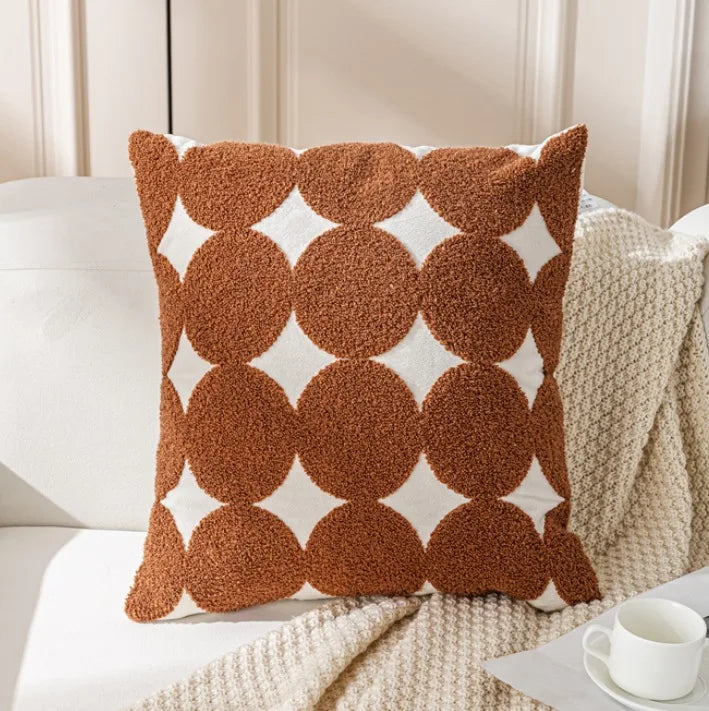 Coussin décoratif avec motif de cercles rouges sur fond blanc, posé sur une couverture beige.