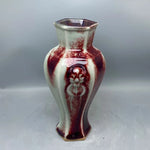 Un vase décoratif à la forme hexagonale et aux motifs colorés en rouge et blanc, dégageant un style unique et artisanal.