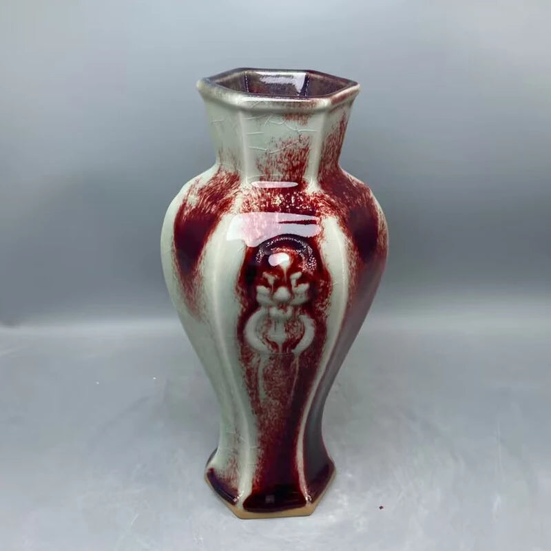 Un vase décoratif à la forme hexagonale et aux motifs colorés en rouge et blanc, dégageant un style unique et artisanal.