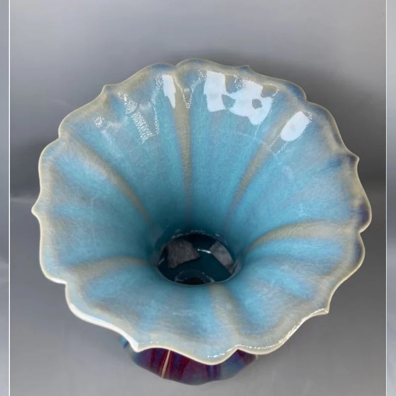 Une élégante fleur céramique en bleu clair et blanc, avec un centre foncé, présentée sur un fond gris.