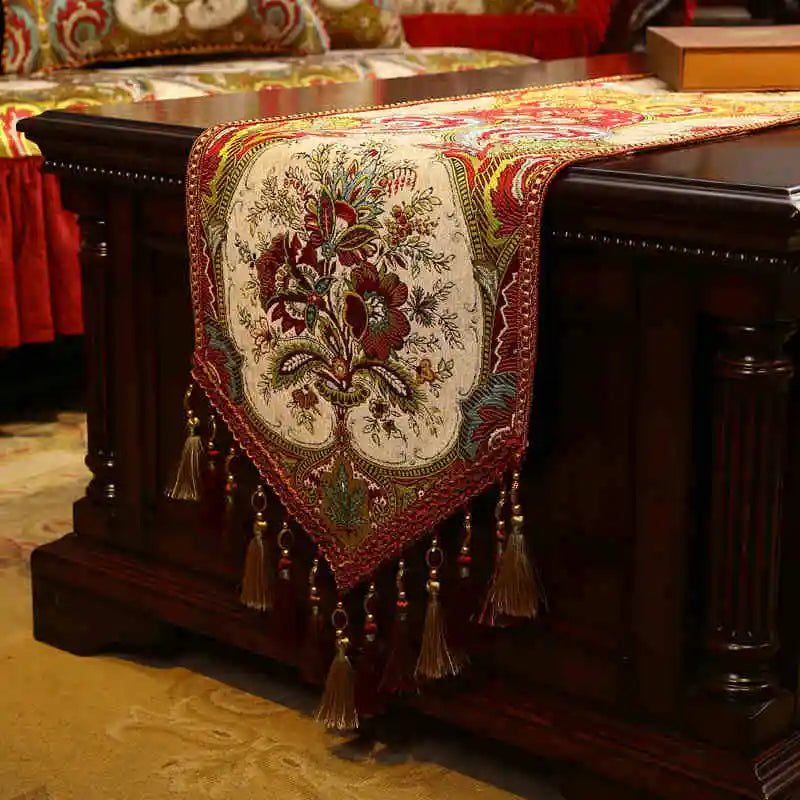 Un chemin de table orné de motifs floraux colorés, agrémenté de pompons et de franges, décorant élégamment un meuble en bois sombre.