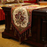 Cette élégante nappe décorative sur un coffre en bois sombre met en valeur un motif floral brodé de couleurs chaudes, créant une ambiance chaleureuse et raffinée.