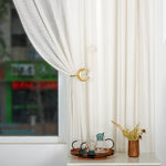 Le rideau blanc translucide avec l'accent doré en forme de lune crée une ambiance douce et paisible, complétée par le plateau en bois et les accessoires de décoration dans le coin de la pièce.