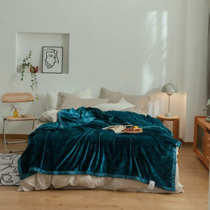 Une chambre confortable avec un lit douillet recouvert d'un plaid en velours bleu profond, une table de chevet en bois, un cadre avec une illustration artistique et une plante d'intérieur qui apportent une touche décorative.