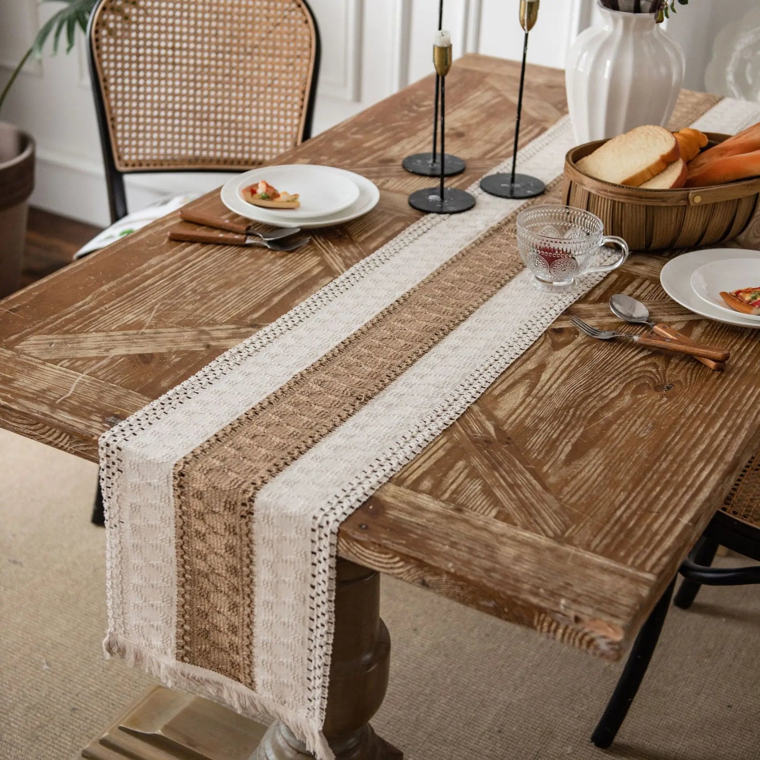 Une table en bois rustique avec une nappe en dentelle beige, des bougies, des verres et une assiette avec un plat sur la surface, créant une ambiance chaleureuse et accueillante.