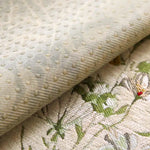 Gros plan sur un motif floral tissé avec des points brillants sur un tissu crème, créant une texture et un design intéressants.