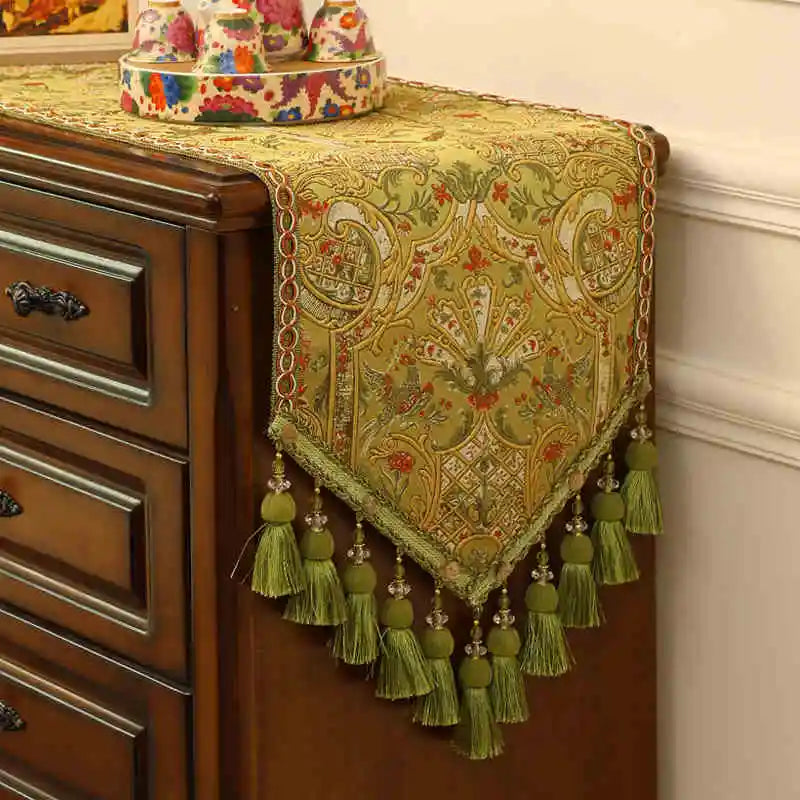 Un magnifique tapis de table orné de motifs floraux dorés et de glands verts décorant avec élégance la commode en bois sombre.