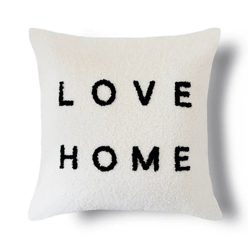 Un coussin décoratif blanc avec le texte "LOVE HOME" en noir.