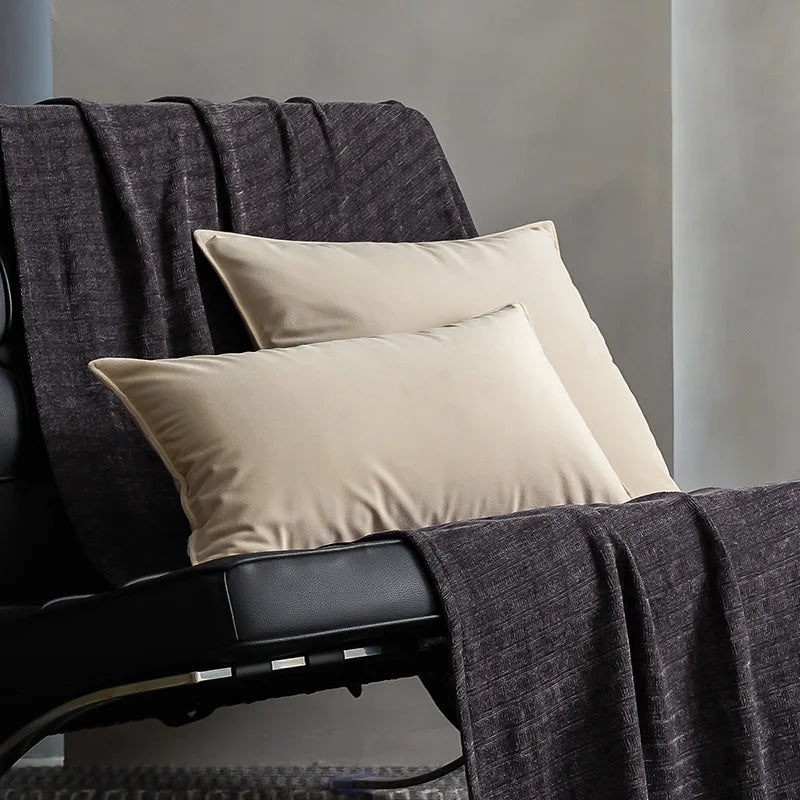 Un sofa gris foncé avec des oreillers blancs beiges et une couverture en tissu gris, dans un environnement sombre et épuré.