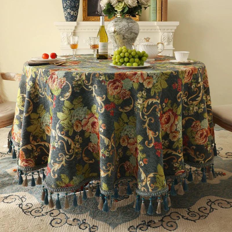 Une belle table décorée avec un magnifique nappage fleuri, une bouteille de vin, des verres, des raisins et un bouquet de fleurs, créant une ambiance chaleureuse et accueillante.
